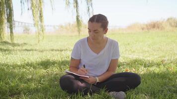 a woman sitting in the grass writing on her notebook video