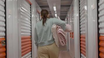 a woman carrying pillow and blanket is walking through a storage unit video
