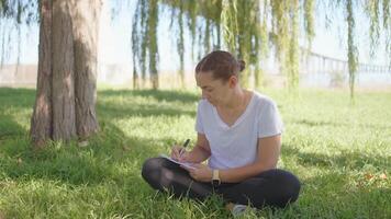 a woman sitting in the grass writing on her notebook video