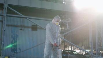 een Mens in een beschermend pak is staand in voorkant van een gebouw sproeien ontsmettingsmiddel video