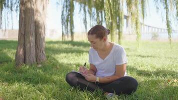 a woman sitting in the grass writing on her notebook video