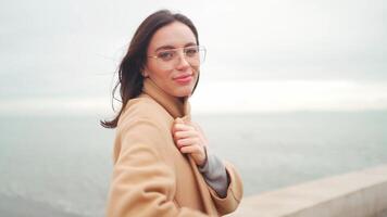 a woman in glasses and a coat standing near the ocean video