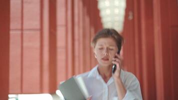 a woman in a white shirt talking on a cell phone video