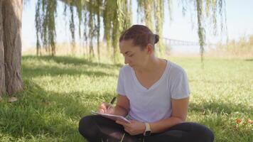 a woman sitting in the grass writing on her notebook video