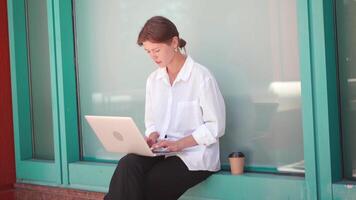 a woman sitting on a ledge with a laptop video