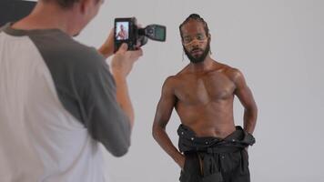 un masculino modelo es haciendo Sesión de fotos sesión en frente de un blanco antecedentes video