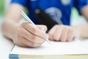 asiático Adolescente estudiante escribir tarea, estudiar lección para examen en línea aprendizaje educación. foto