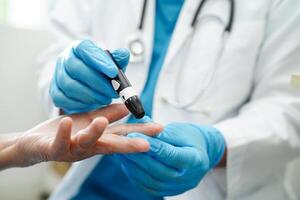 Asian doctor using lancet pen on senior patient finger for check sample blood sugar level to treatment diabetes. photo