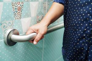 Asian woman patient use toilet support rail in bathroom, handrail safety grab bar, security in nursing hospital. photo