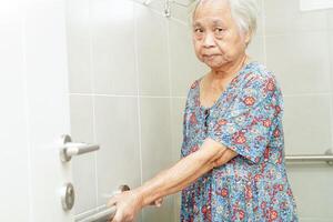 Asian elderly old woman patient use toilet support rail in bathroom, handrail safety grab bar, security in nursing hospital. photo