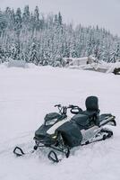 Black snowmobile stands on the snow near a snowy forest photo