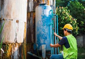 asiático hombre ingeniero controlador el calidad de agua lugares operando industrial agua purificación o filtración equipo antiguo cemento tanques para acuerdo agua en agua fábrica foto