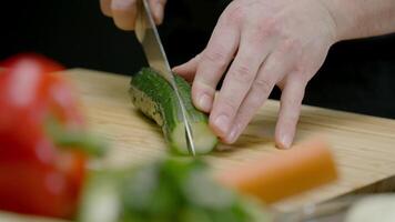 Male chef's hands cut a cucumber with a knife on a cutting board video