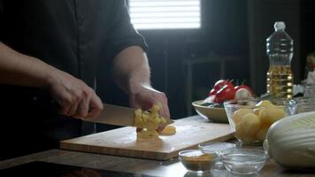 The cook cuts the potatoes into cubes on a cutting board using a knife. video