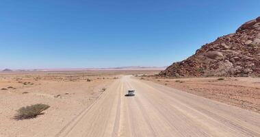 Drone video of a moving vehicle on a lonely gravel road through the desert