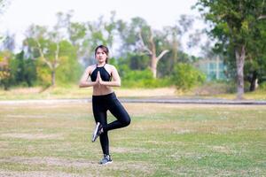 retrato de un joven asiático mujer en pie y hacer ejercicio en naturaleza, durante el verano o primavera tiempo. trabajando mujer son haciendo yoga a tramo su piernas y músculos. vacío espacio para entrando texto. foto