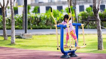 asiático niña en columpio en parque, rodeado por naturaleza en patio de juegos, sonriente dama disfrutando al aire libre ejercicio en soleado verano día, pequeño hija disfrutar y teniendo divertido estilo de vida fin de semana actividad en verano. foto