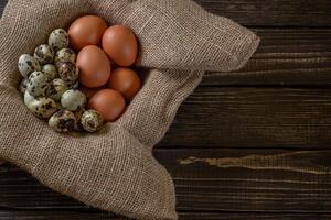 Fresco pollo y codorniz huevos en un cesta en un bolsa, de madera tabla.selectiva atención foto