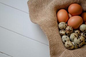 Fresco pollo y codorniz huevos en un cesta en un bolsa, de madera tabla.selectiva atención foto