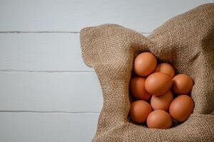 Fresh chicken eggs in a basket on a sack, egg day, wooden table.Selective focus photo