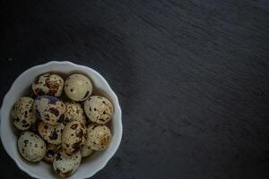 Fresh quail eggs in white plate on black stone, selective focus photo