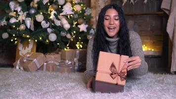 familia Navidad, divertido fiesta, permanecer a hogar, nuevo año celebracion. un mujer abre un regalo caja acostado en el piso en Navidad víspera video