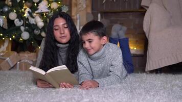 Familie Weihnachten, Spaß Party, bleibe beim heim, Neu Jahr Feier. Mama und Sohn lesen ein Buch im das Abend Nächster zu das Weihnachten Baum video