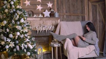 família Natal, Diversão festa, fique às lar, Novo ano celebração. feliz mulher lendo uma livro enquanto sentado dentro uma cadeira perto a Natal árvore video