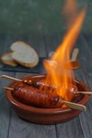 típico Español tapa chorizo en fuego en un loza de barro maceta foto