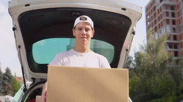 Moviente y entrega de fabricado bienes. un empleado sostiene un caja en su manos y soportes siguiente a un coche lleno con parcelas video