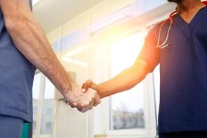 Two young Doctors shaking hands to each other. Multiracial team of young doctors. photo