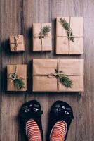 Feet with warm winter socks and cat slippers standing in front of Christmas gifts. top view. photo