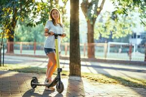 sonriente mujer paseos eléctrico scooter o e-scooter en ciudad parque a puesta de sol. hembra utilizando eléctrico transporte en urbano parque foto