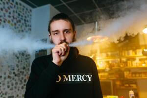 Young Men with beard vaping and releases a cloud of vapor. close-up. photo