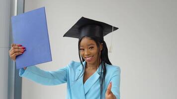 a afro-americano graduado mulher dentro uma luz azul clássico terno e uma quadrado mestrado chapéu poses alegremente e energeticamente e danças com uma diploma dentro dela mão. mulher com superior Educação video