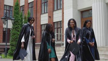 contento laureati di un' Università o Università di africano americano nazionalità nel piazza Vestiti gettare su piazza cappelli di il maestro verso l'alto. alunno scambio programma. più alto formazione scolastica per donne nel Europa video