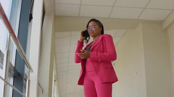 glamoureus Afrikaanse Amerikaans bedrijf dame in roze pak pratend Aan cel telefoon in de kantoor video