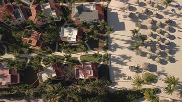 Aerial top view of tourist condominium, beach, and beach umbrellas during sunset on tropical island in Caribbean Sea. Background. Abstract video