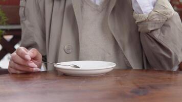 A young woman with a neat manicure in beige and white casual clothes picks up a white porcelain cup of coffee and puts it back on a saucer. Close-up view of hands and cups video