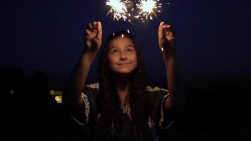 jovem lindo mulher com grandes Sombrio cabelo detém fogos de artifício às noite em a fundo do a cidade e se alegra. lento movimento. hd video