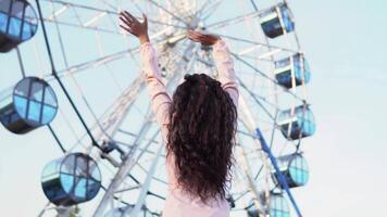 A beautiful young girl waving her friends who are on the Ferris wheel. slow motion video