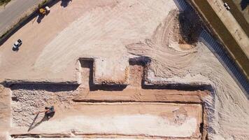 Aerial top view of the construction site. A pit dug for the foundation of a building. View from a drone. Heavy Machinery and Construction Workers are Working in the Area. Zoom in video