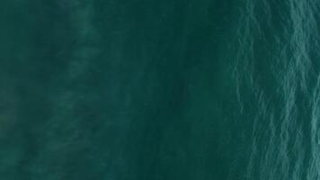 Waving ocean. Foamy turquoise water surface sparkling. Aerial top shot vertical video