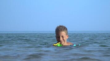 A little boy bathes in the sea and plays with paper boats. He is smiling and happy. 4K video