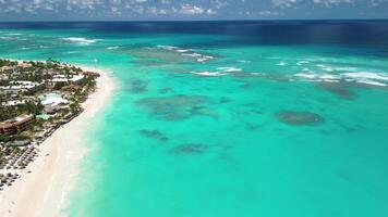 zangão Visão do azul caribe mar com coral recife e litoral com branco areia de praia e casas cercado de verde tropical floresta com nublado céu em uma ensolarado dia video