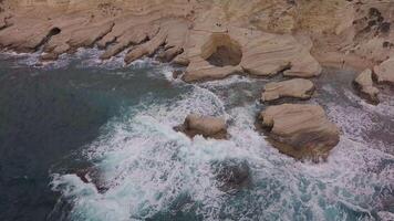 aéreo ver de estrellarse olas en rocas paisaje. tormenta olas en el Mediterráneo mar. 4k video