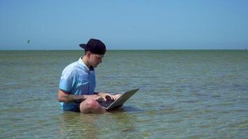 un hombre trabajos en vacaciones. el chico en el mar con un ordenador portátil. el chico es trastornado y lanza el computadora dentro el mar. persona de libre dedicación remoto trabajo concepto. 4k video