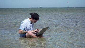 un' uomo lavori su vacanza. il tipo nel il mare con un' il computer portatile. libero professionista a distanza opera concetto. 4k video