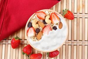 natural yogurt with homemade granola, strawberries and nuts in ceramic bowl on a table top view photo