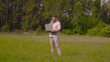 Geschäftsmann mit ein Laptop reden auf das Telefon auf das Rasen. beim das sonnig Tag. Freiberufler Fernbedienung Arbeit Konzept. 4k video